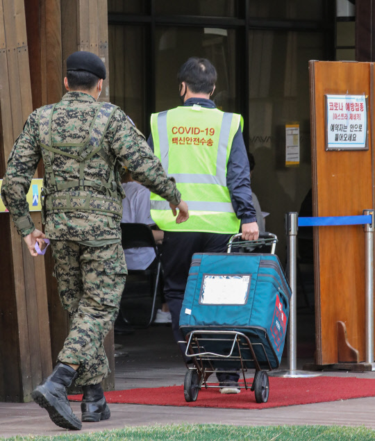 26일 오전 코로나19 백신 수송단 관계자와 경비에 나선 군 관계자가 냉장팩에 담긴 코로나19 백신을 서울 송파구 보건소로 옮기고 있다. <연합뉴스>